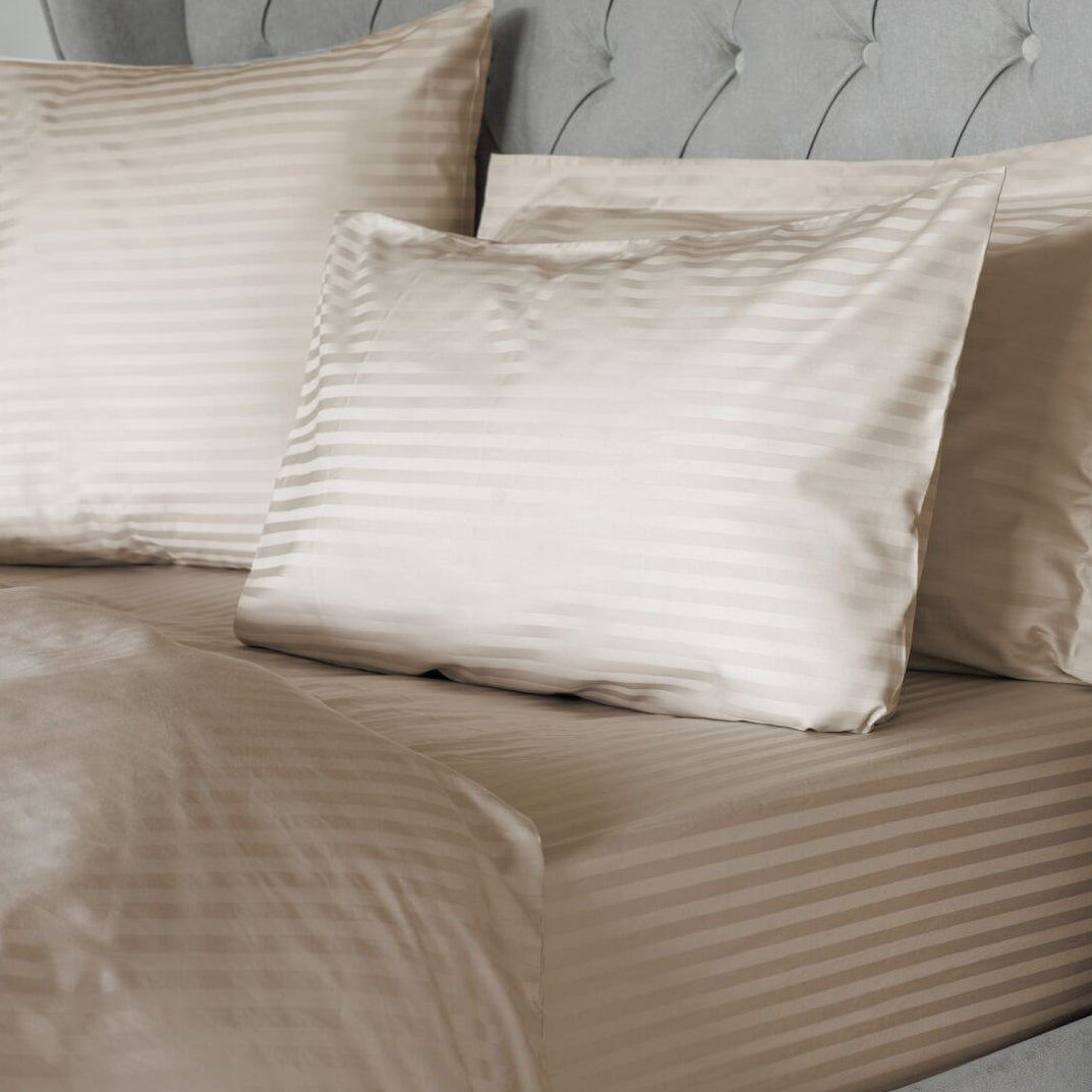 Beige striped bedding and pillows on a bed with a gray upholstered headboard.