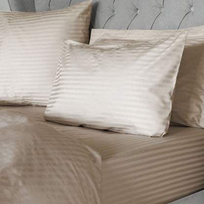 Beige striped bedding and pillows on a bed with a gray upholstered headboard.