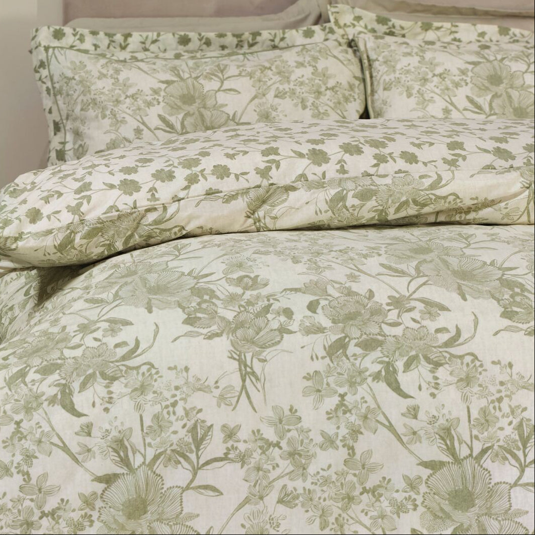 Floral patterned bedding set on a bed in a bedroom setting with a green chair and plant.