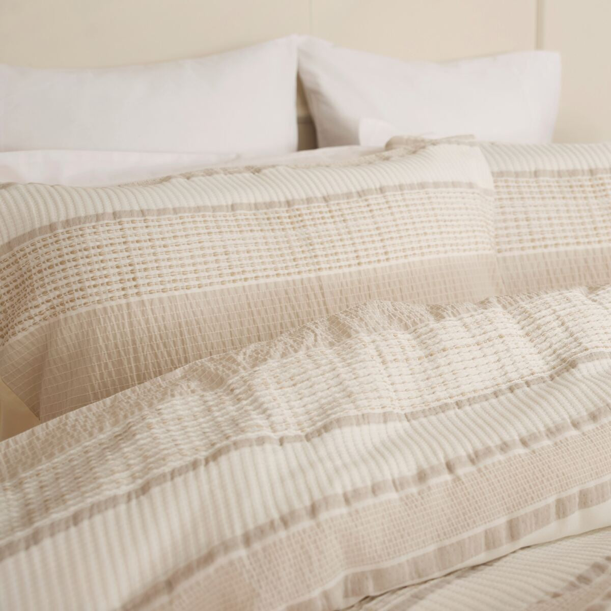 Beige textured comforter on a bed with pillows and a plant in the background