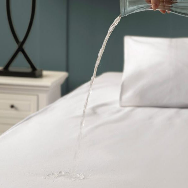 White comforter being poured over a white pillow on a bed with a blurred background.