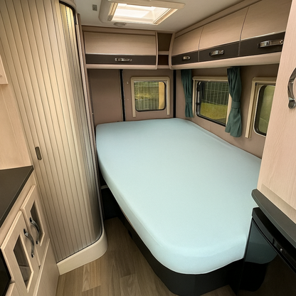 Compact bedroom interior of a vehicle with a bed, windows, and cabinets.