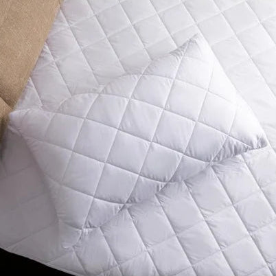 White quilted mattress cover on a bed with beige headboard