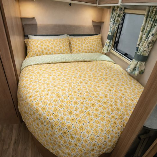 Bed with yellow floral bedding in a compact living space, possibly inside a vehicle or small home.